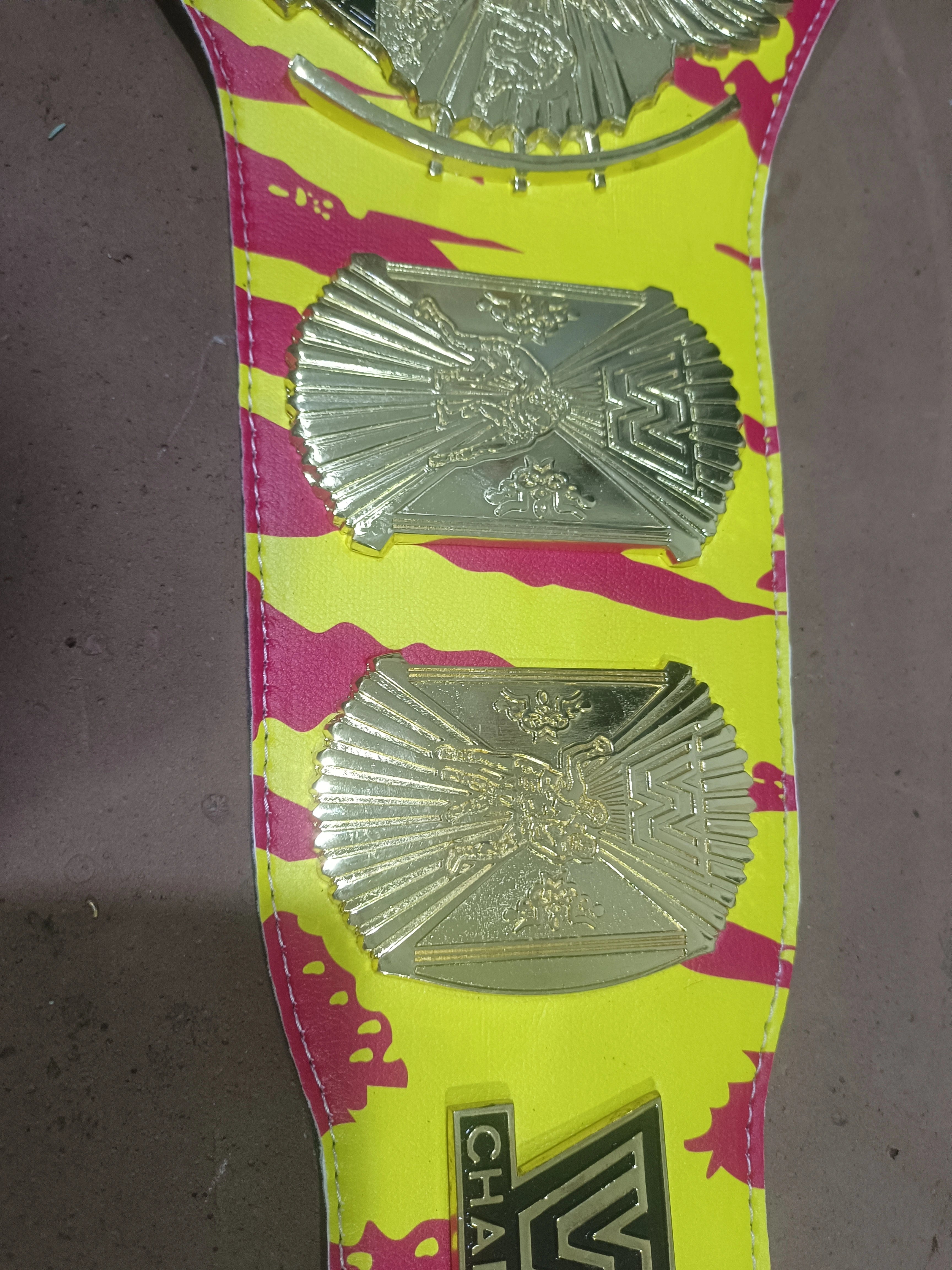Close-up of gold side plates on a yellow and pink Hulk Hogan championship belt strap.